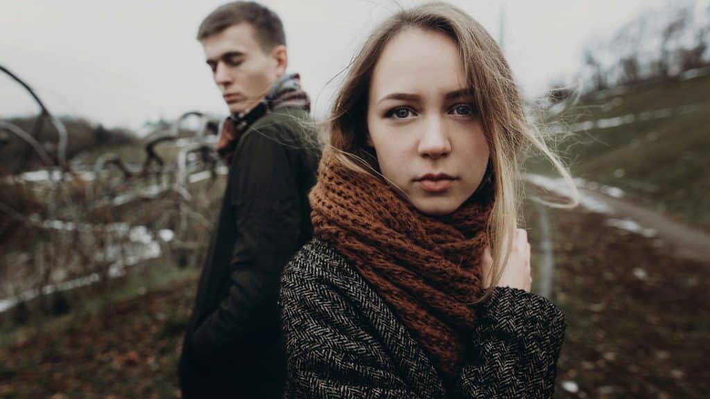 A man staring at a woman over his shoulder as they stand outdoors.