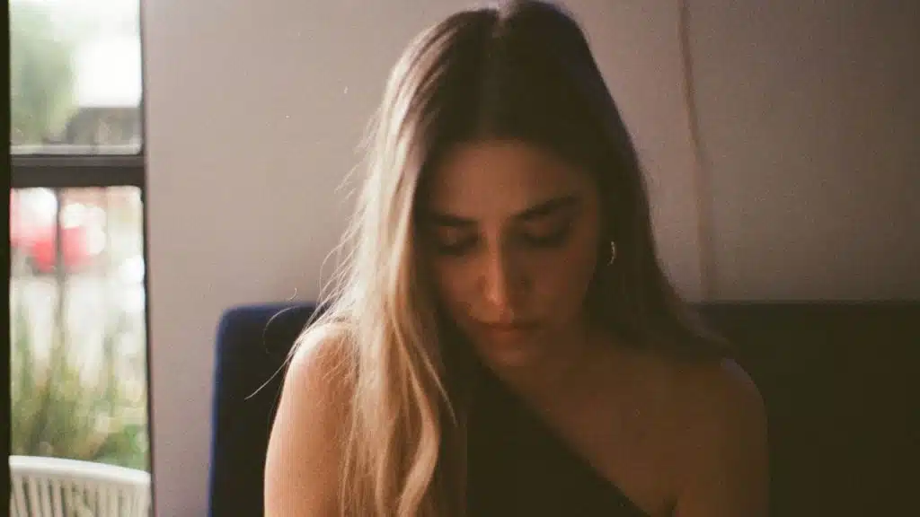 Woman with long hair looking down, possibly reading, in soft window light.