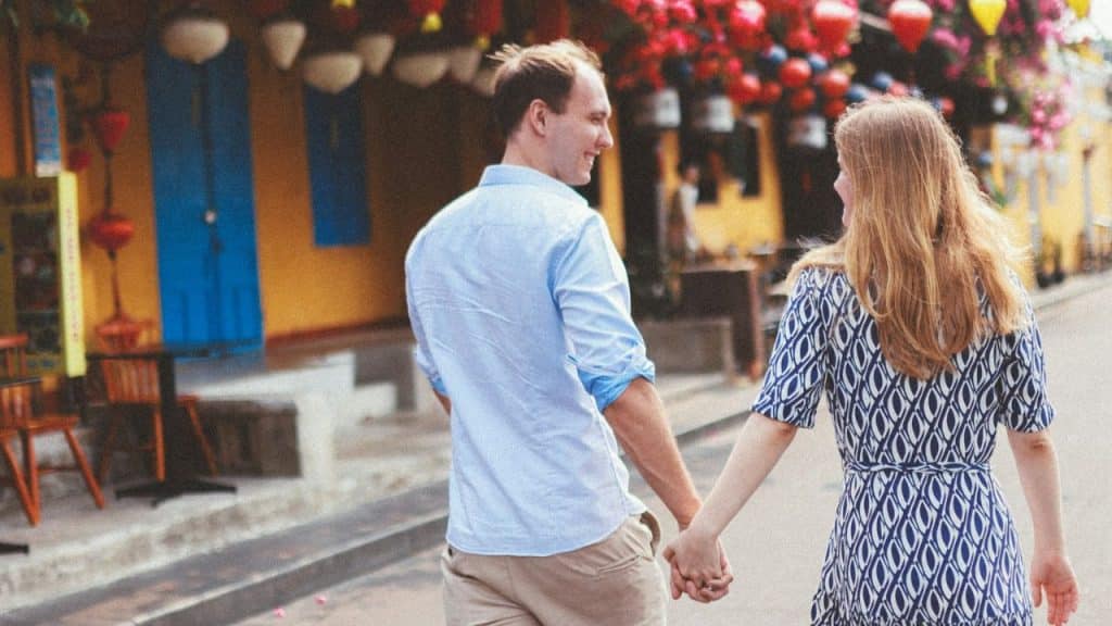 Couple holding hands and walking away from the camera on a colorful street.