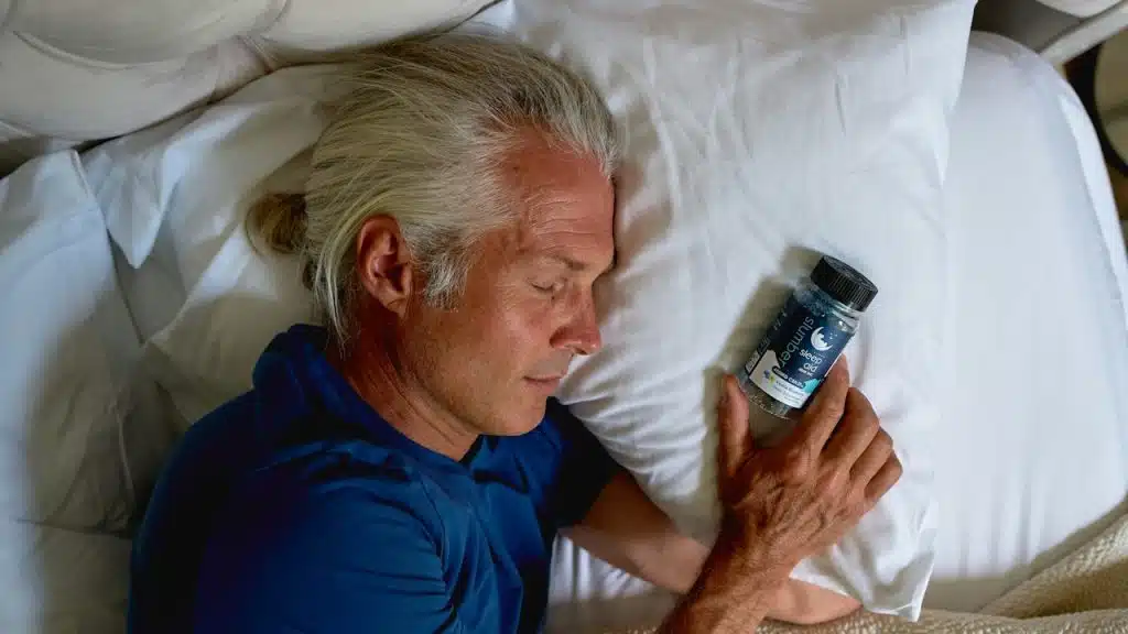 A man lying on a bed holding sleeping pills.