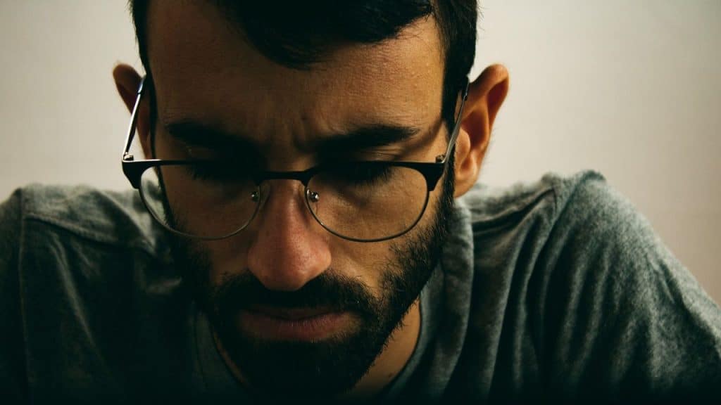 Close-up of a man with a beard and glasses looking intensely down.