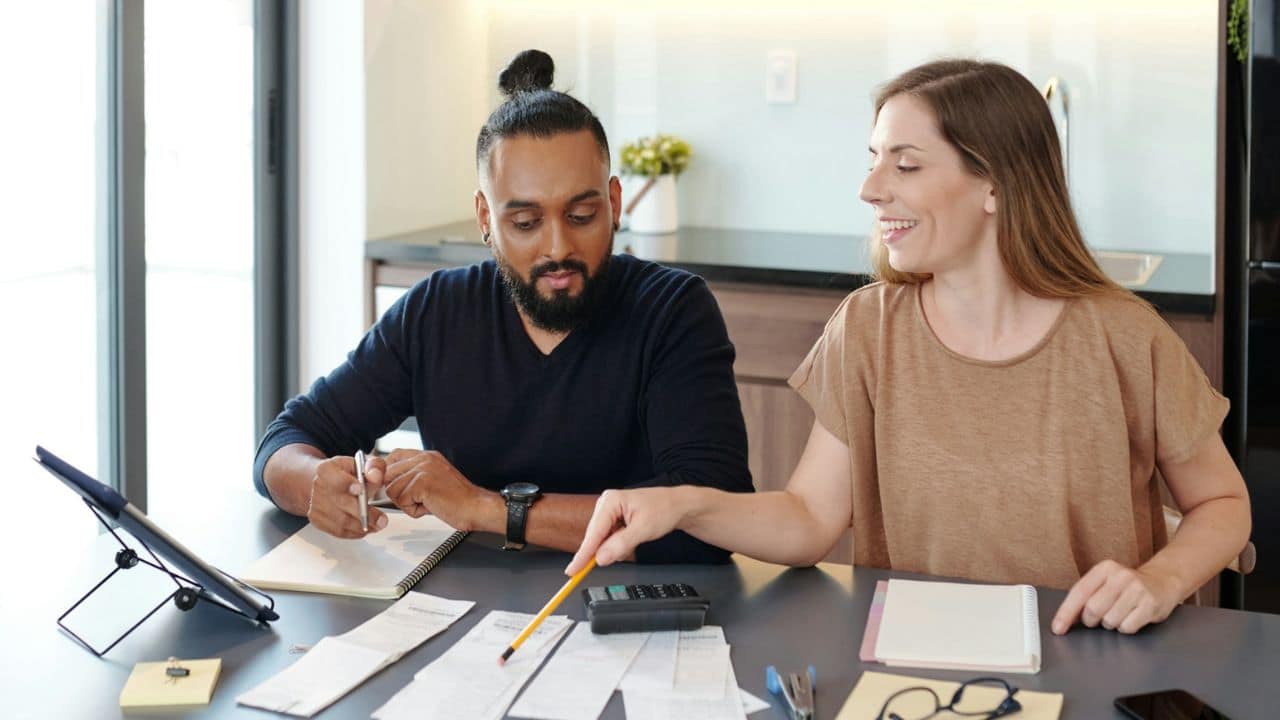 A couple reviews receipts on a table; the woman points with a pencil.
