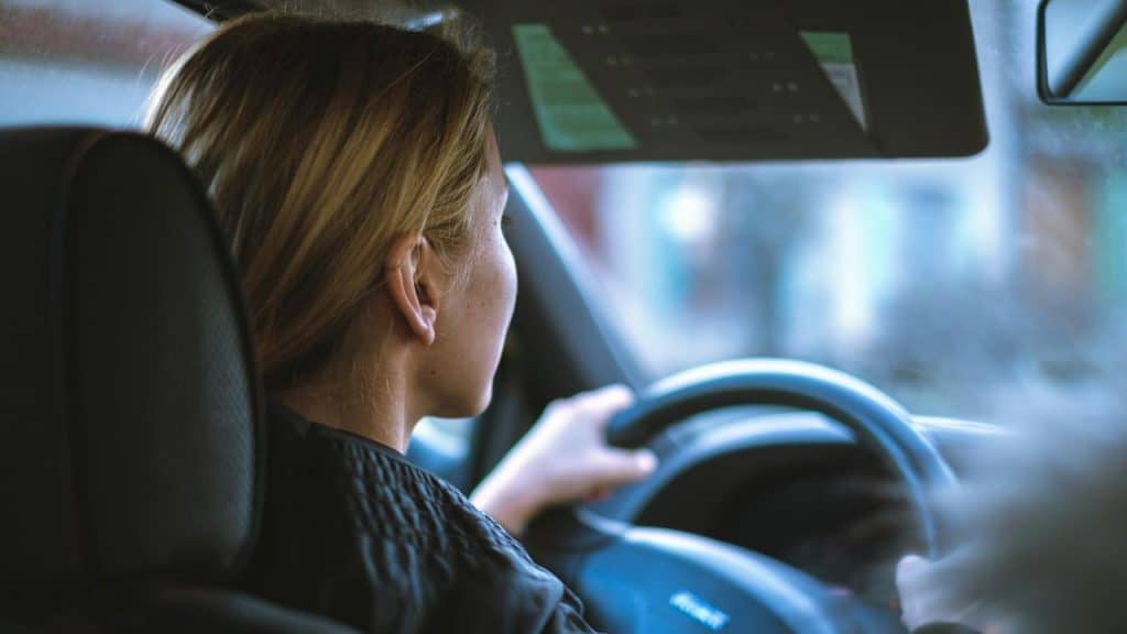 A woman driving a car with two hands on the steering wheel.