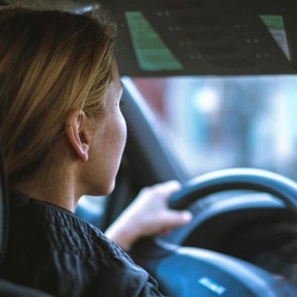 A woman driving a car with two hands on the steering wheel.