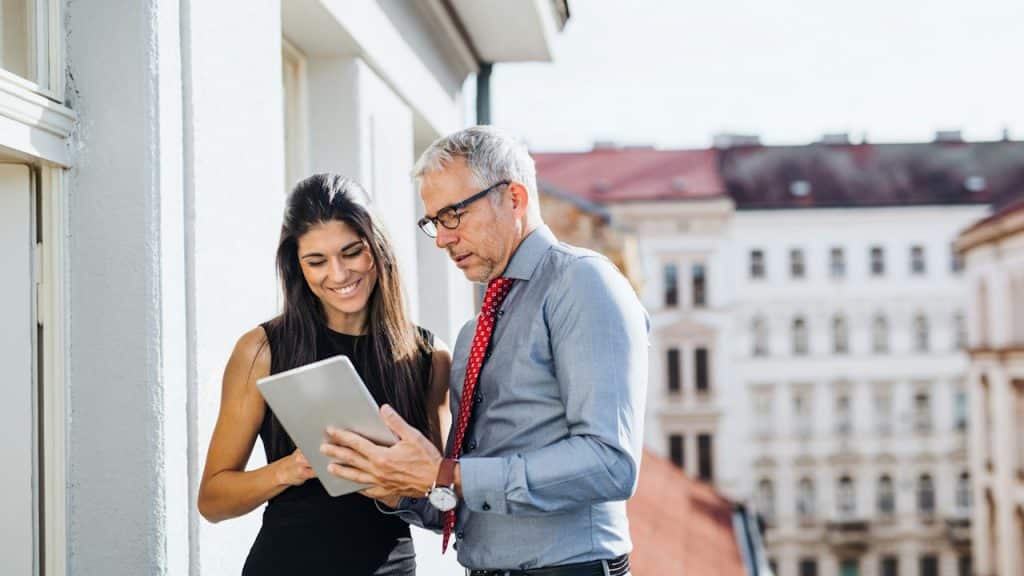 A man and woman, business partners, with a tablet, standing on a terrace in an office.
