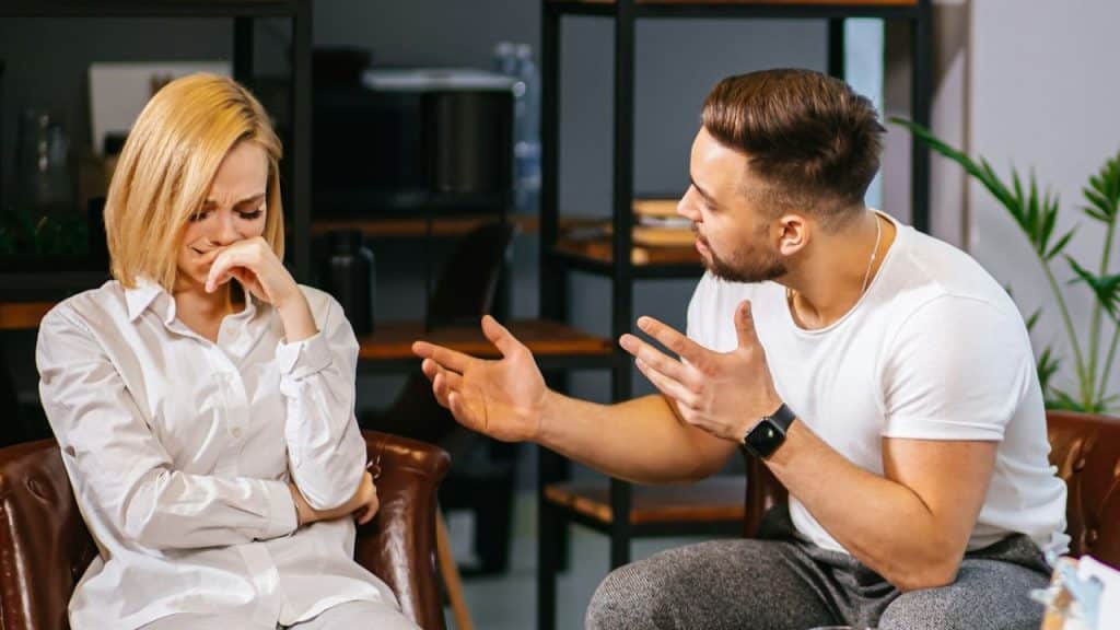 Man gestures aggressively at a crying woman who is holding her hand to her face.