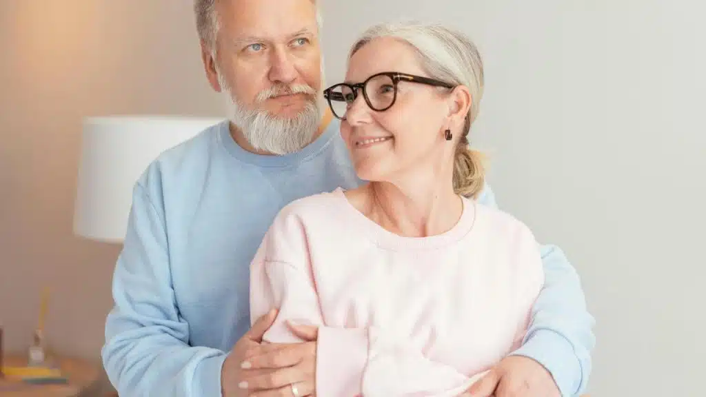 A senior couple standing close together, embracing warmly.