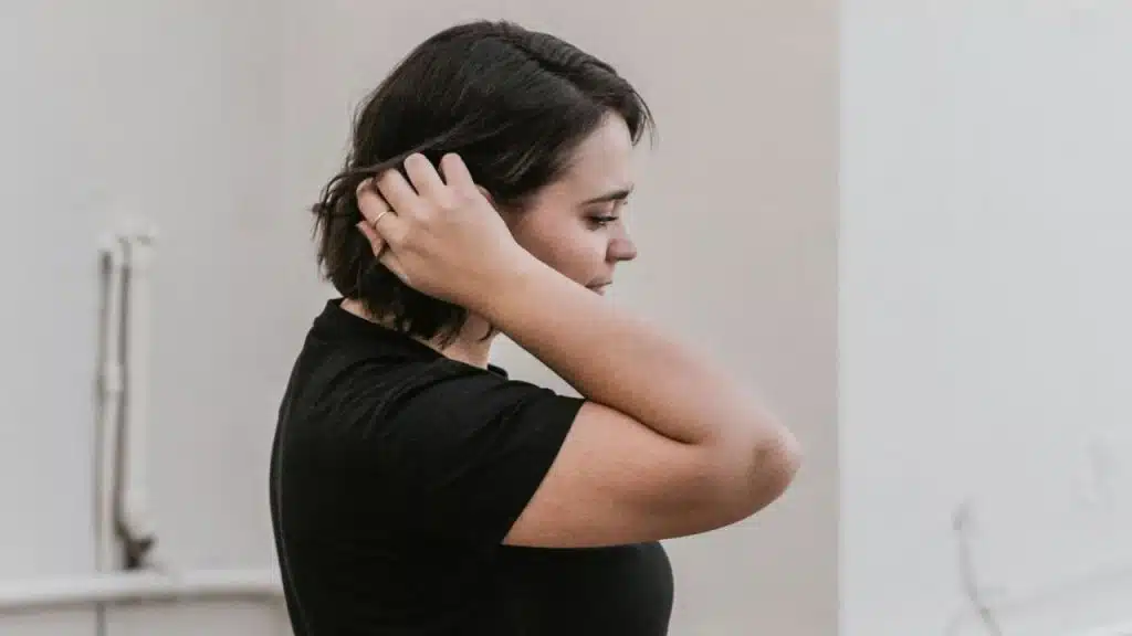 A woman in a black shirt reaches up to adjust the hair at the back of her head.
