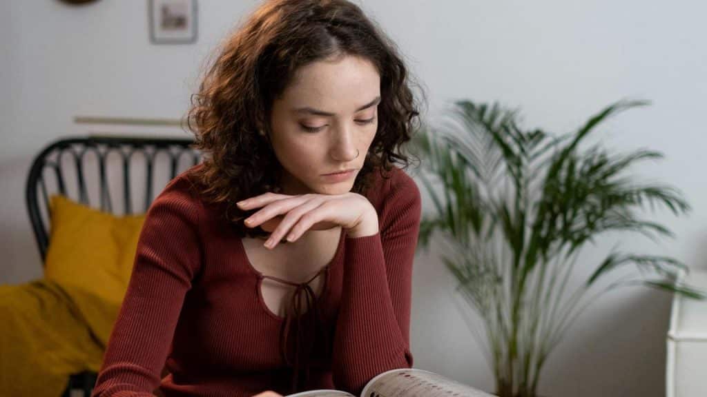 A woman reading a book with her chin resting on her hand in a cozy room.