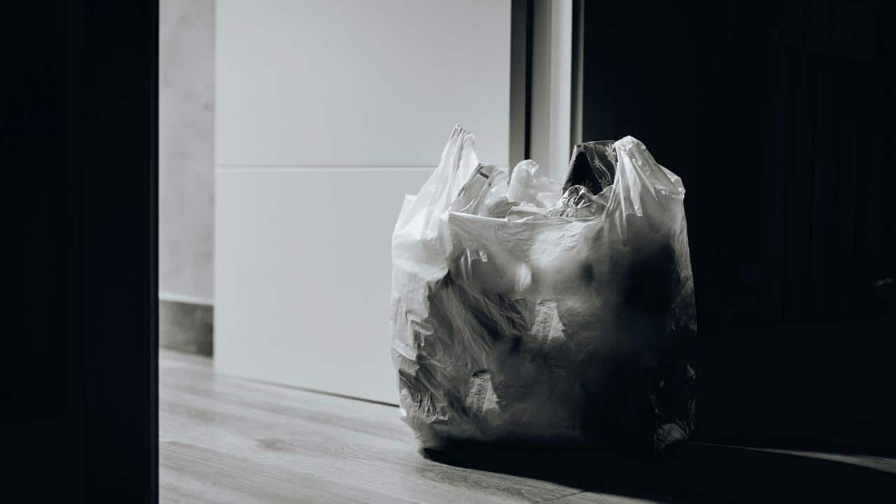 A plastic trash bag full of garbage placed on the floor near a doorway.