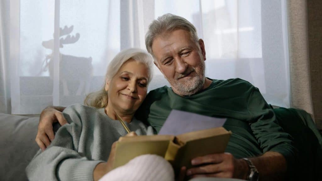 A couple relaxing on a couch while reading a book together.
