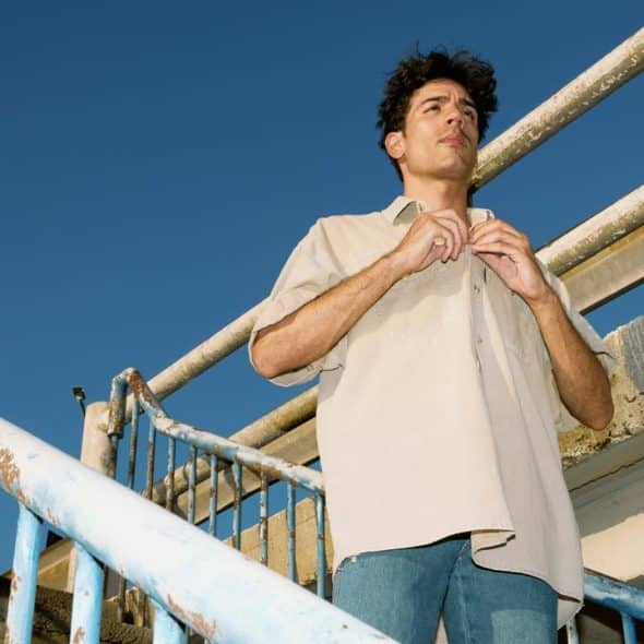 A man buttoning his shirt on an outdoor staircase under a clear blue sky.