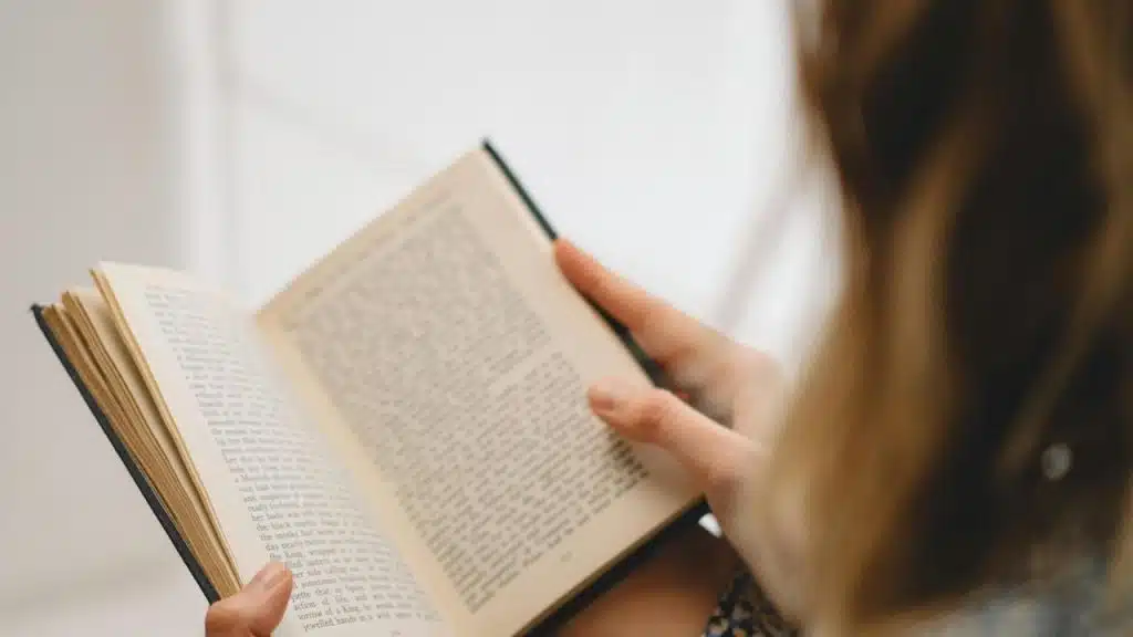 A person holding and reading an open book indoors.