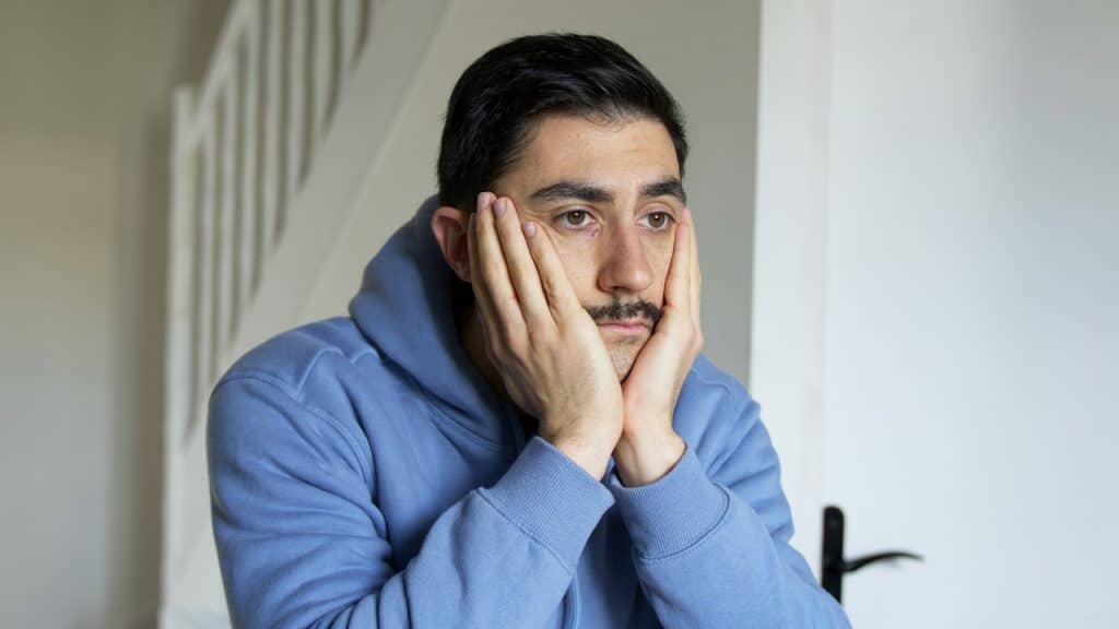 A mustached man holding his face in his hands and looking worried.
