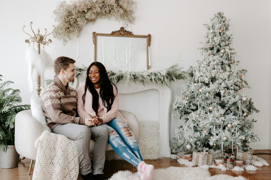 A couple sitting on the couch, in front of the Christmas tree.