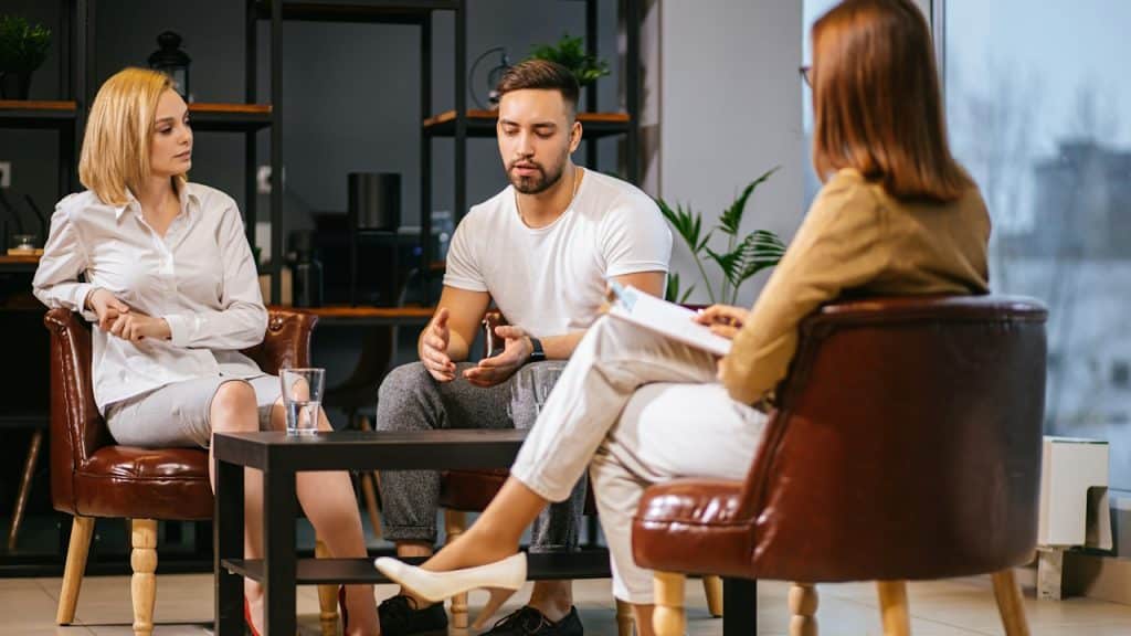 A couple discussing something while sitting in a therapist’s office.