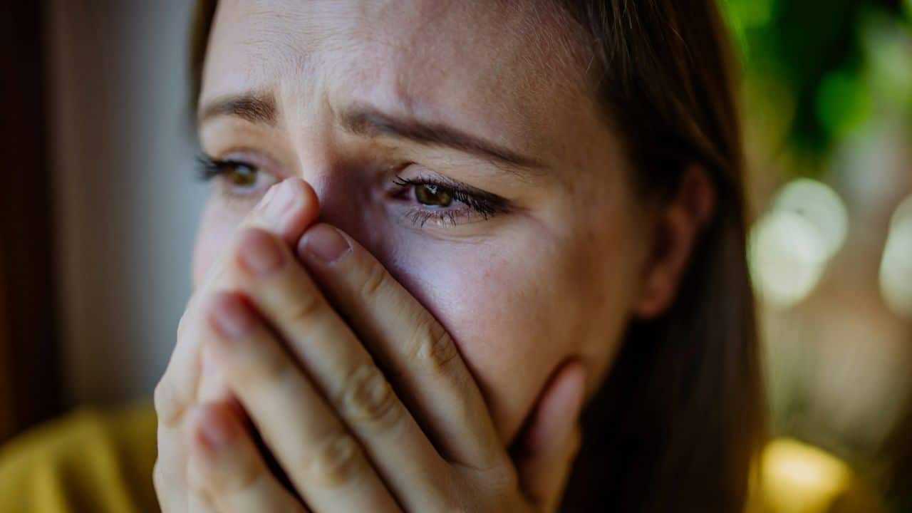 A distressed woman covers her mouth and nose with her hands, eyes teary.