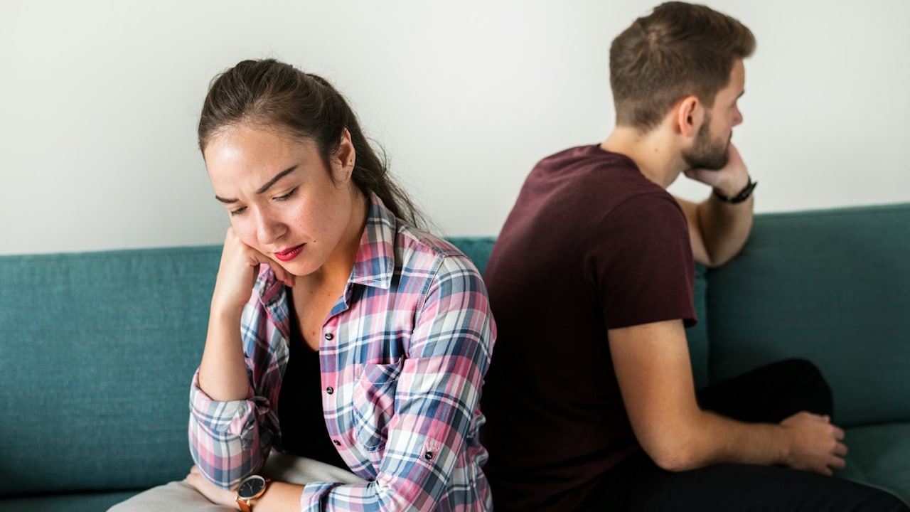 An unhappy couple sitting back-to-back on a couch after an argument.