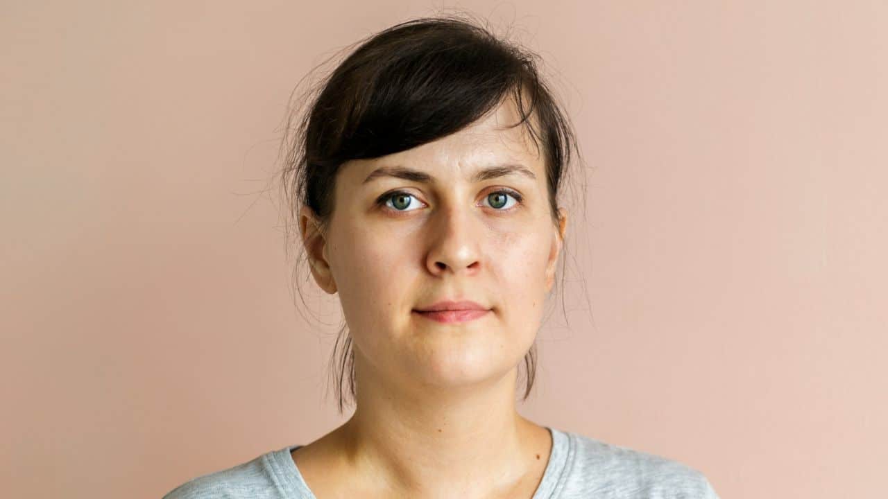 A close-up studio shot of a woman with dark hair against a pink background.