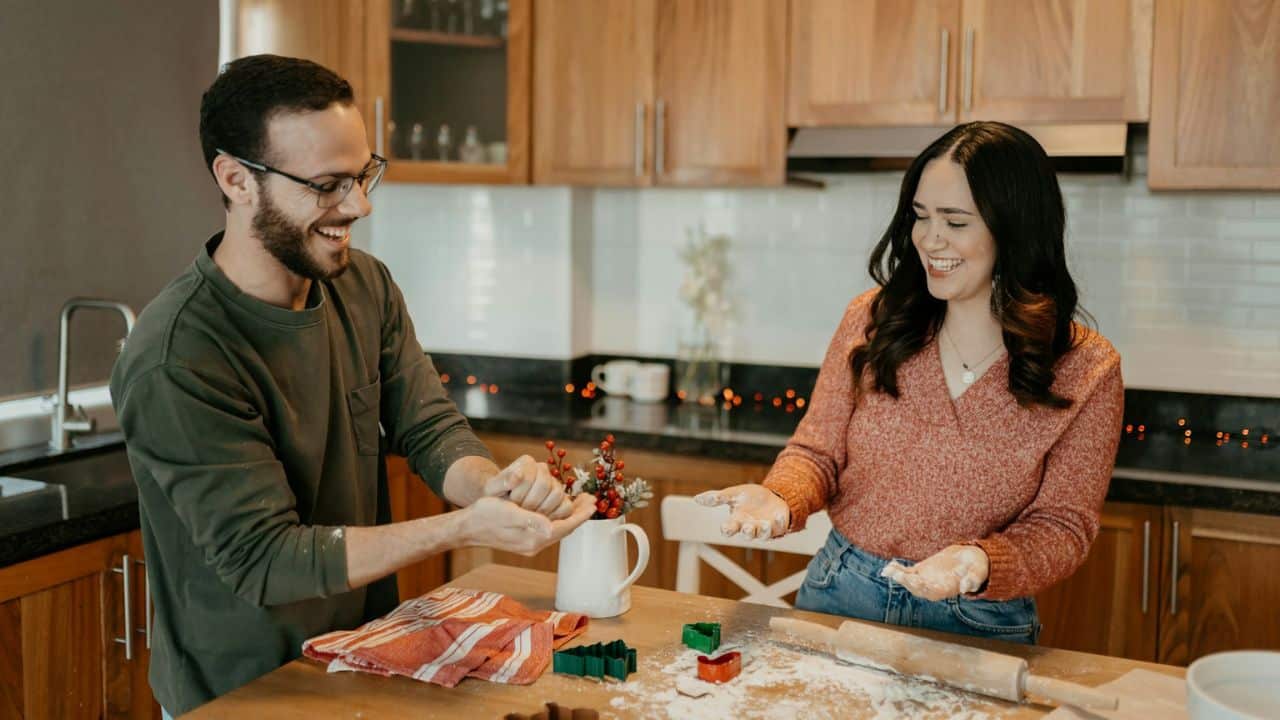 Couple laughing in a kitchen, kneading dough and covered in flour while baking.