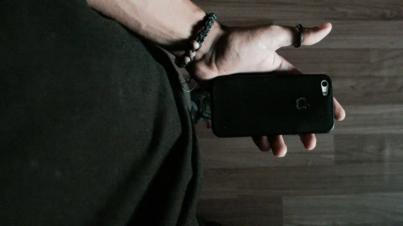 A close-up of a hand holding a black phone with the Apple logo face-up.