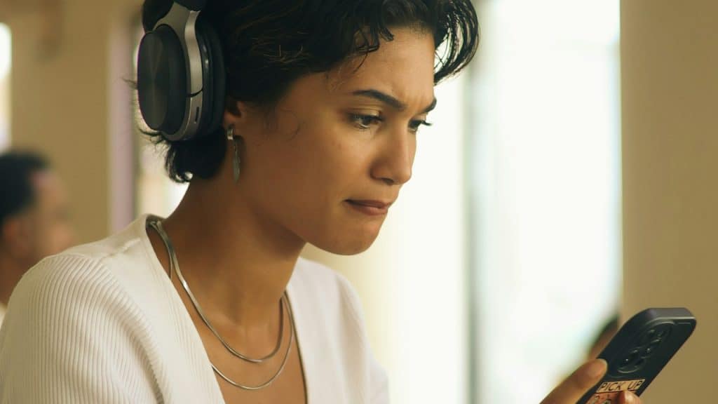 A young woman wearing headphones looks at her phone.