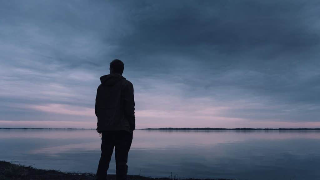 A silhouette of a man standing near a body of water.