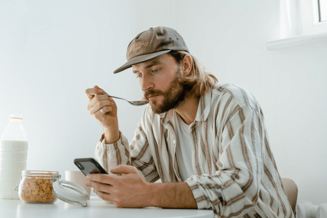 A man sitting at a table while eating and using a phone