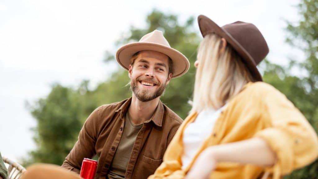 Smiling man in a hat talking to a woman in a yellow shirt outdoors.