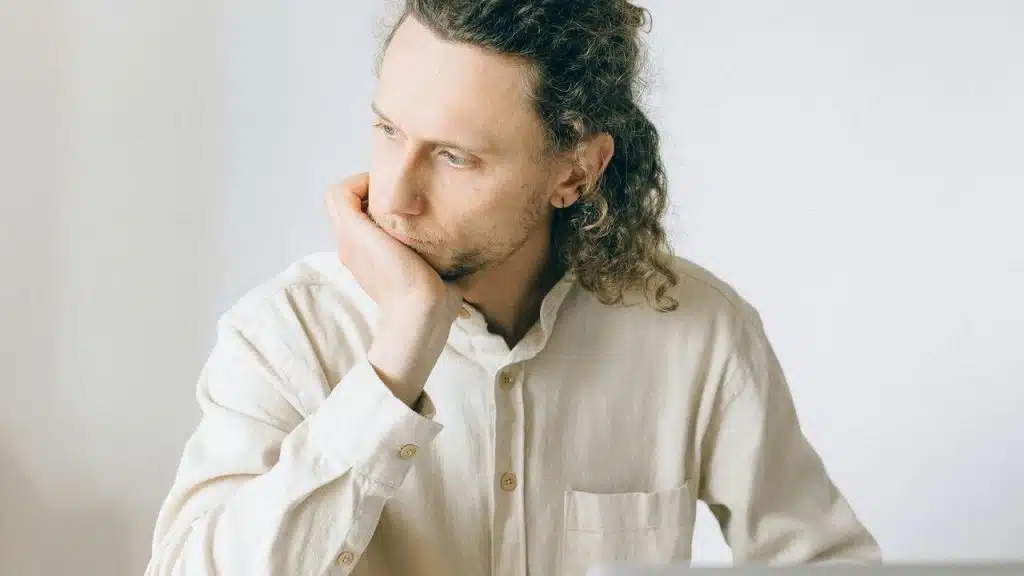 A person with curly hair resting their chin on their hand, looking thoughtful.