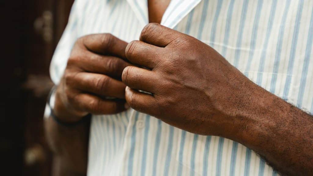 A man buttons up a striped shirt.