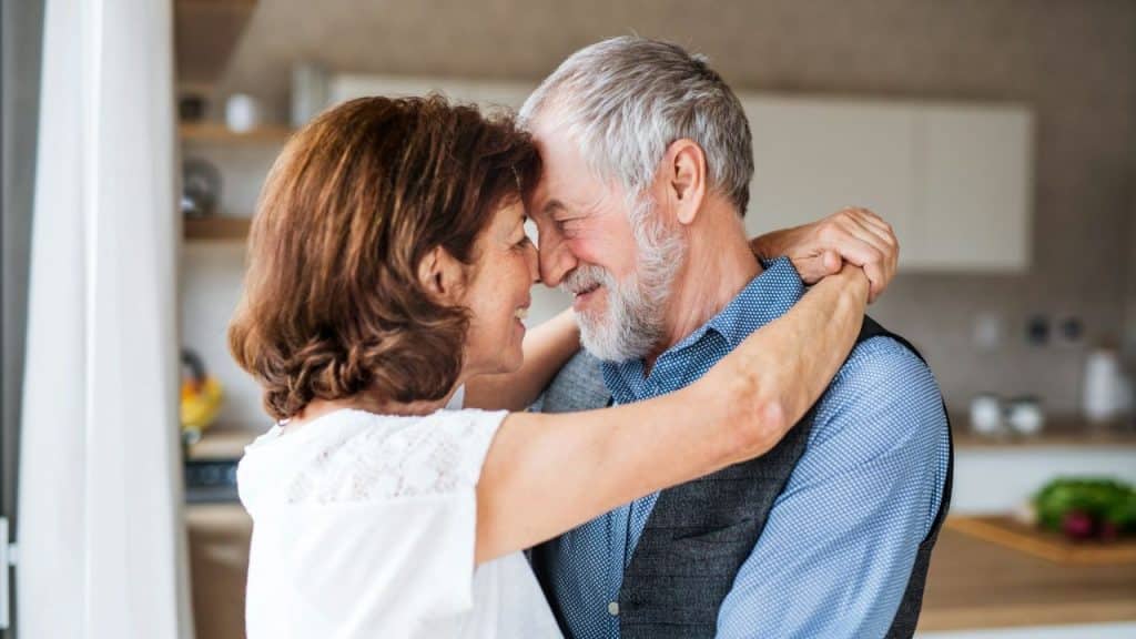 Elderly couple happily embracing, looking at each other in a bright, modern kitchen.