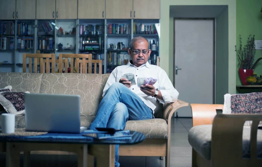 A man holding money and the laptop and calculator are on the table.