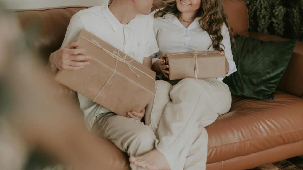 A couple sitting on a couch holding wrapped gifts.