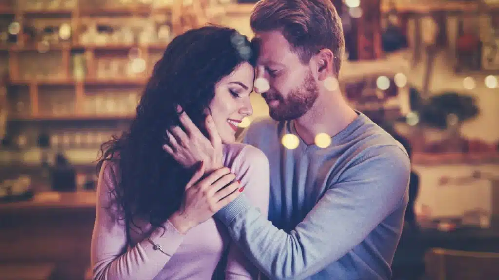 Couple embracing tenderly in a dimly lit, blurred setting that looks like a cafe.