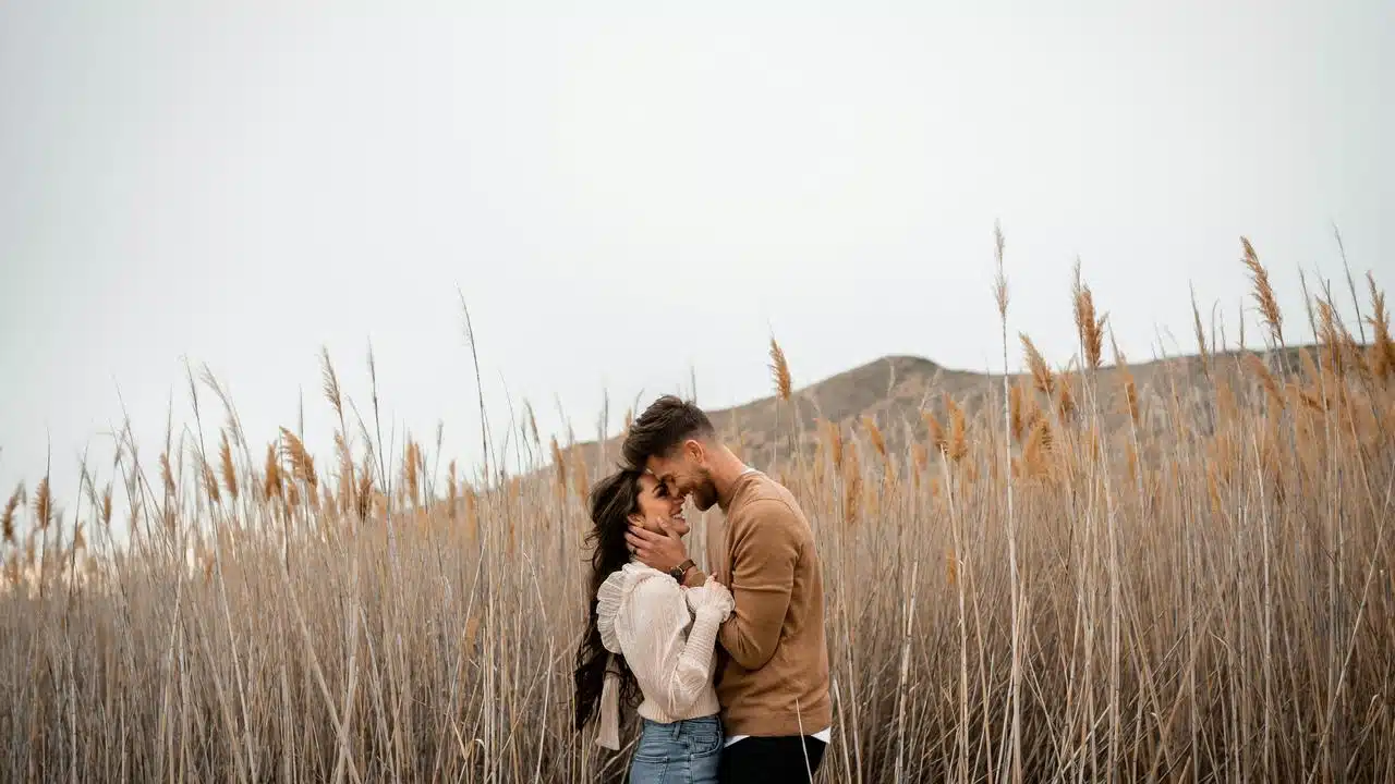 A couple standing closely together in a field of tall grass.