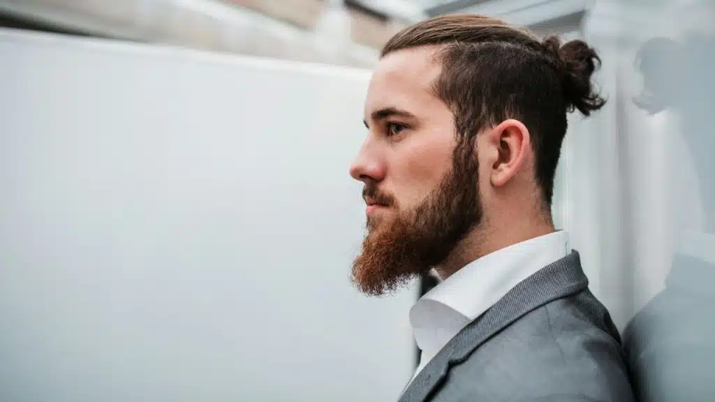 Man with neat hair and beard in a grey jacket and white shirt, looking sideways.