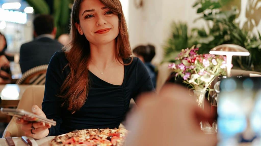 A woman smiling at a café table with a plate of food and a phone.