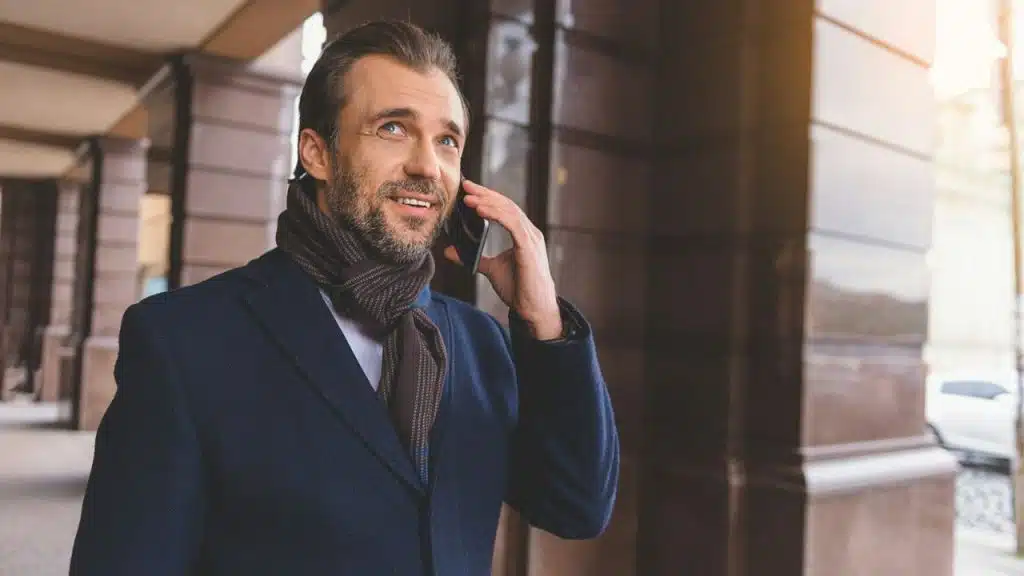 Middle-aged man in a suit and scarf talking on a cell phone outdoors.
