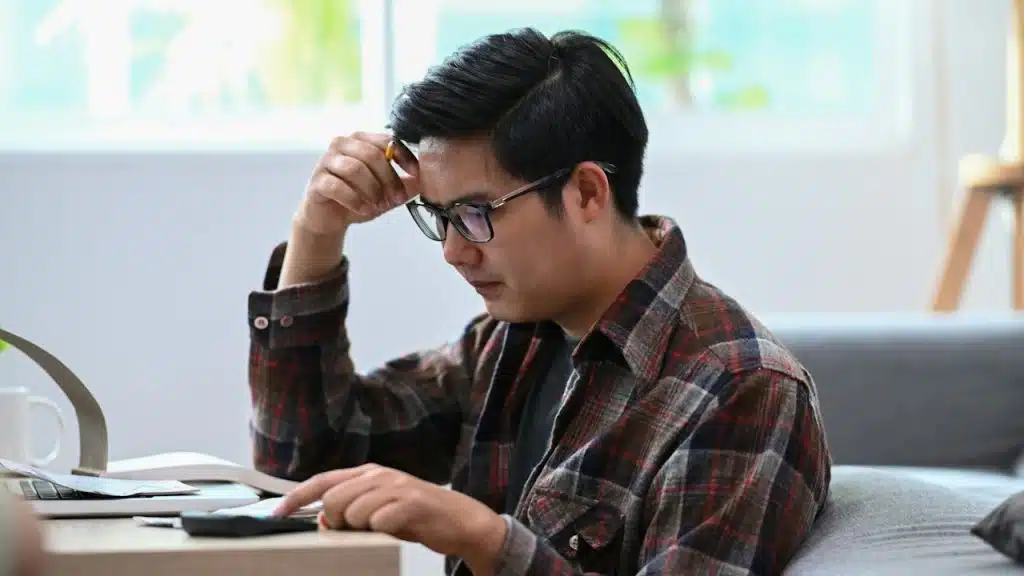 A stressed man using a calculator and managing household finances in the living room.