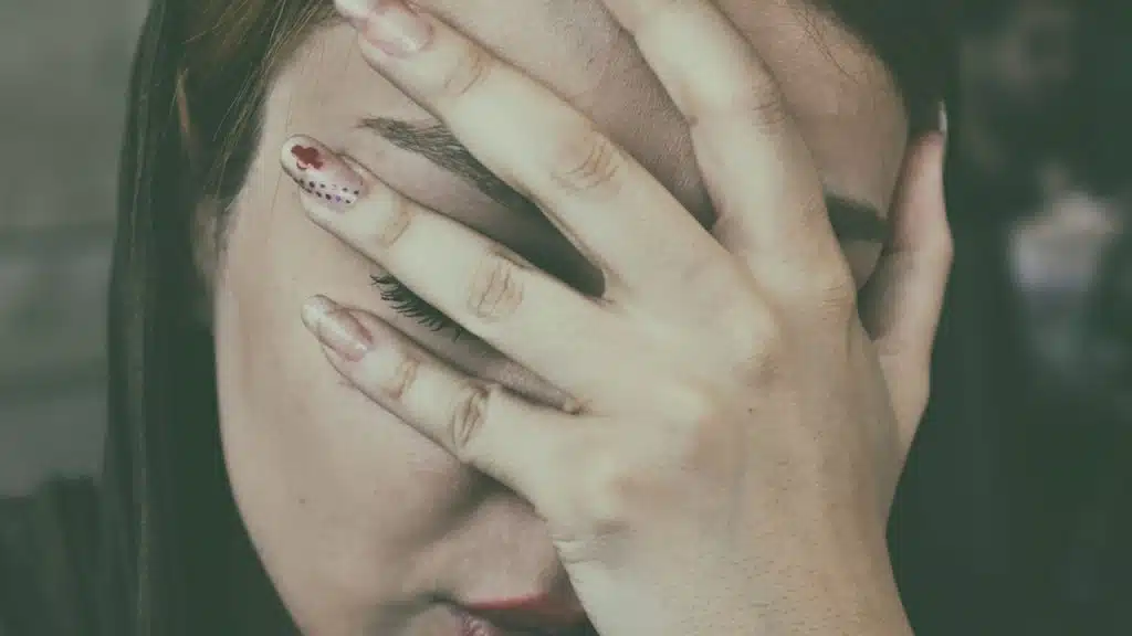 A closeup of a woman covering her face with her hand.