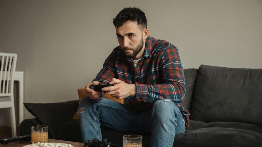 Man with a beard and flannel shirt sits on a sofa playing a video game.