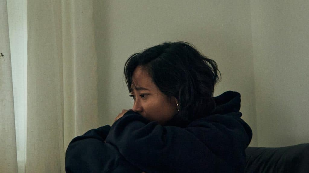 A woman sitting by a window, looking sad and deep in thought.