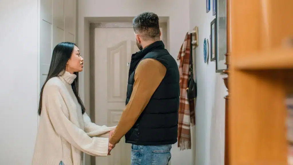 A woman holding a man’s hand while speaking to him in a hallway.