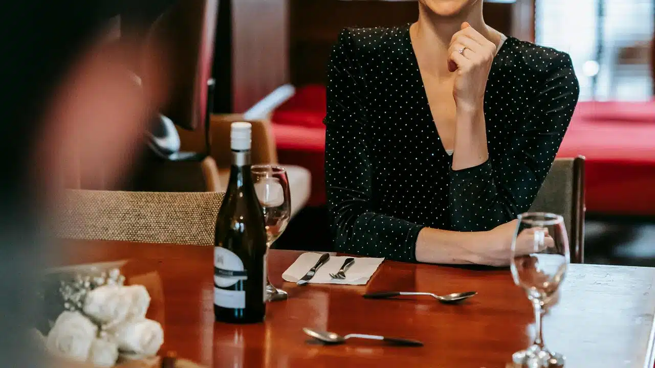 A woman in a black polka dot dress sitting at a restaurant table with wine.