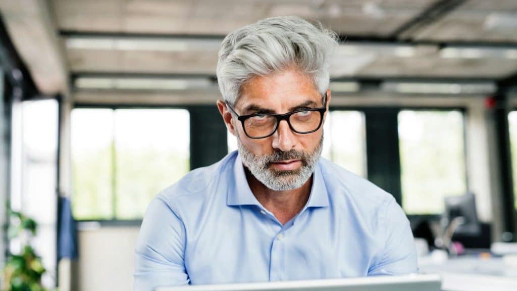 Middle-aged man with gray hair and glasses looks intensely over a silver screen.