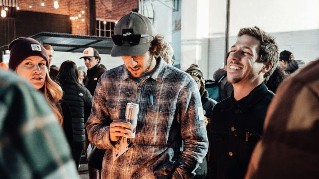 A man wearing a black shirt laughs, while a woman looks embarrassed in a crowd with other people.