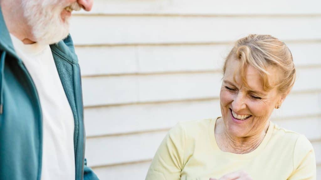 A senior couple standing outside, smiling warmly at each other.