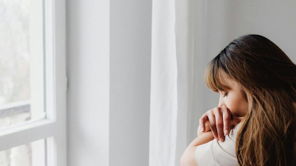 A woman sitting by a window with her arms folded and head resting thoughtfully.