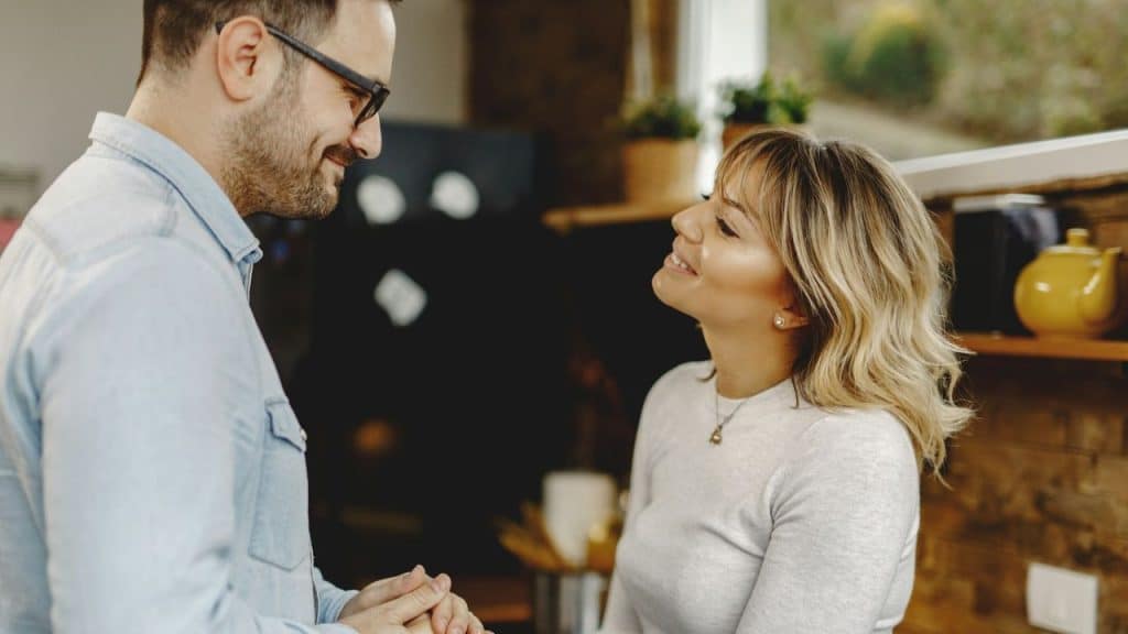 A man with glasses and a beard smiles while looking at a woman in profile.